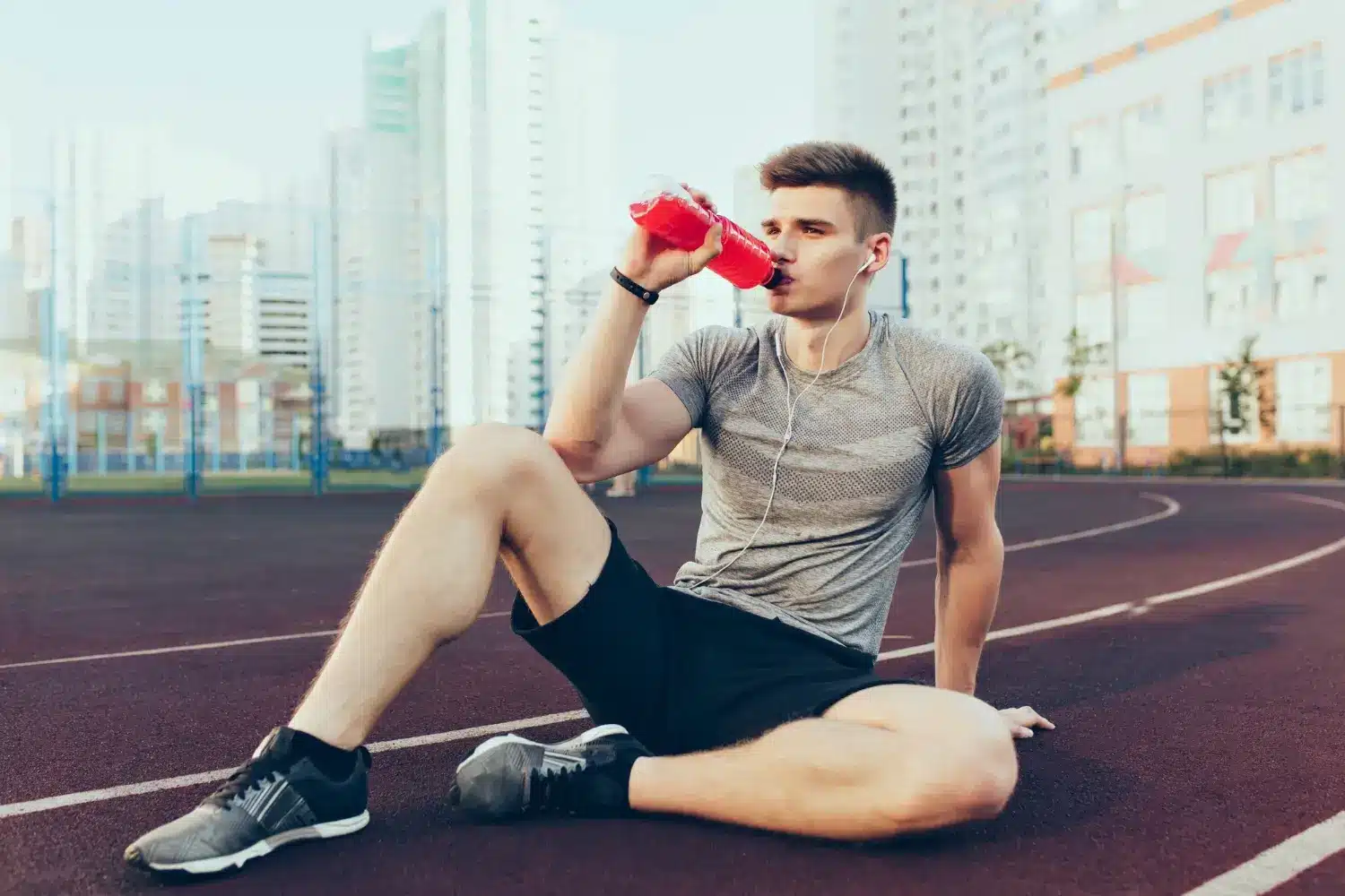atleta bebiendo un bidón de agua en una pista de atletismo.
